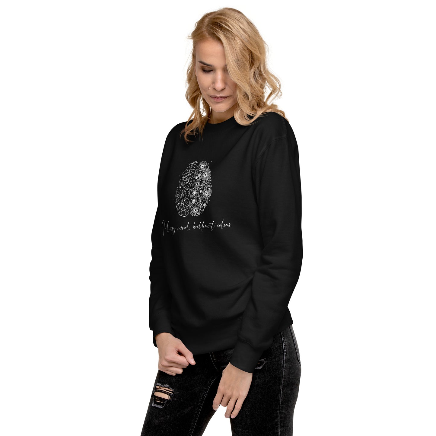 A blond woman wearing a black unisex premium sweatshirt featuring a sleek illustration of a brain with flowers blooming from it. The text 'Messy Mind, Brilliant Ideas' is written in a delicate script underneath the design, symbolizing creativity emerging from chaos