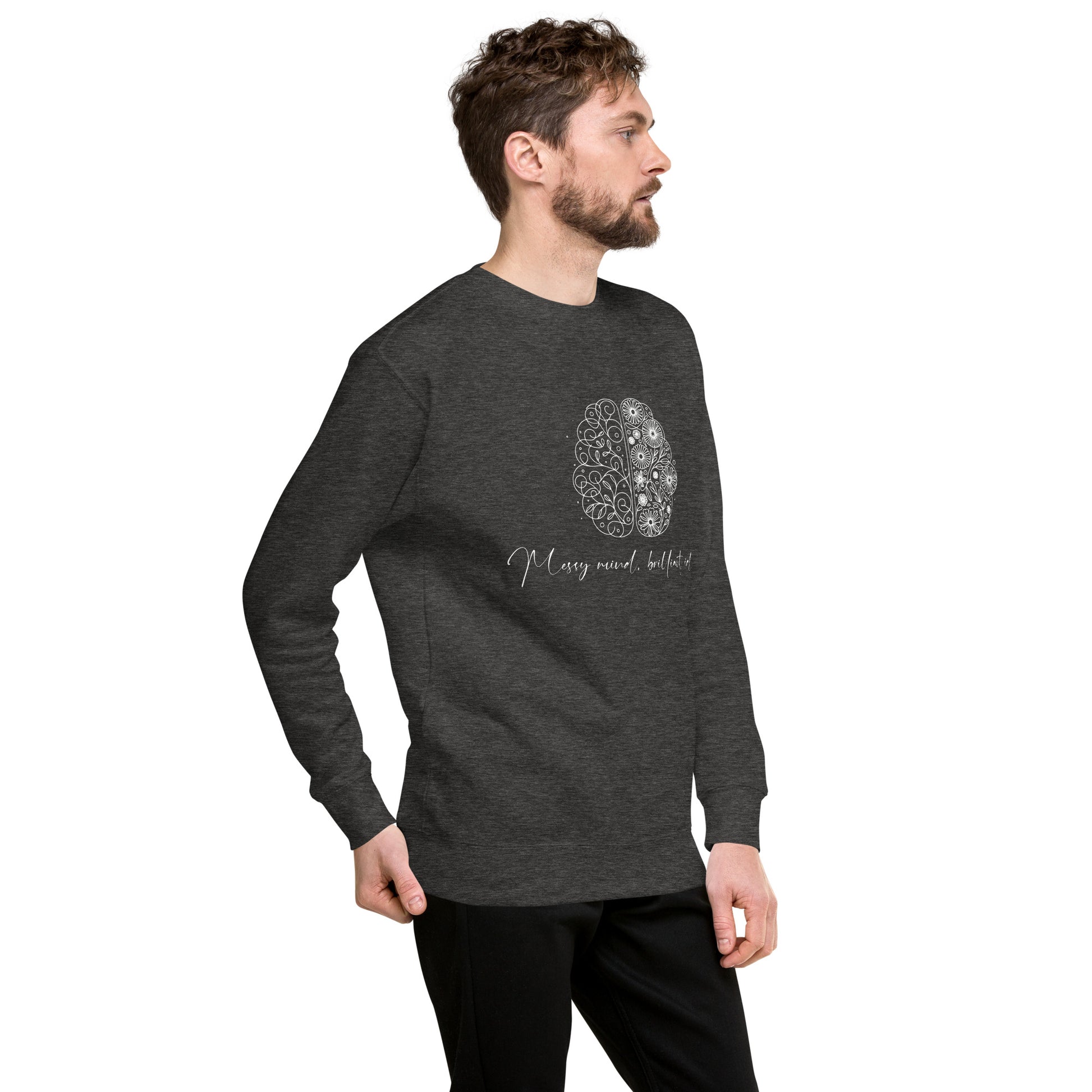 A blond man wearing a charcoal unisex premium sweatshirt featuring a sleek illustration of a brain with flowers blooming from it. The text 'Messy Mind, Brilliant Ideas' is written in a delicate script underneath the design, symbolizing creativity emerging from chaos