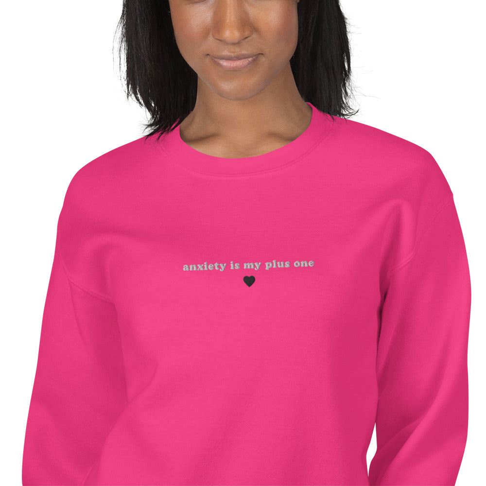 Female model wearing a heliconia (bright pink) embroidered unisex crewneck sweatshirt with 'anxiety is my plus one' text, perfect for mental health awareness and self-expression.