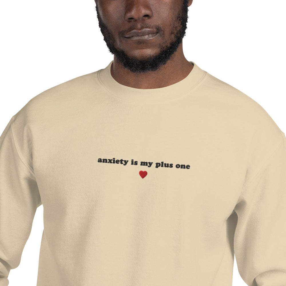 Man wearing a beige embroidered unisex crewneck sweatshirt with 'anxiety is my plus one' text, perfect for mental health awareness and self-expression.